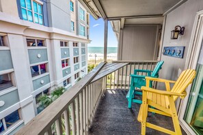 A balcony with a view of the beach, two Adirondack chairs, and a building with multiple windows. - Calm Seasons by the Sea — 2BR Oceanview at Chateau by the Sea, North Myrtle Beach (North Myrtle Beach)