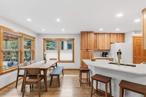 A modern kitchen with wooden cabinets, a white countertop, and a dining area with wooden chairs and a bench. - Wonderful 3-bedroom house in Silverthorne perfect for your getaway (Silverthorne)