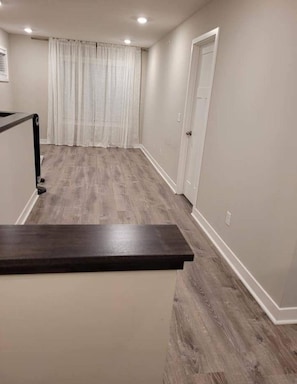 A hallway with a wooden floor, a door on the right, and a window with curtains. - Beautiful & modern townhome! Master bedroom + two bedrooms. (Lakeville)