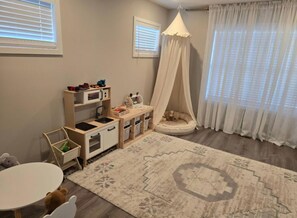 Ein Kinderzimmer mit einer Spielküche, Spielzeug und einem Baldachinbett.