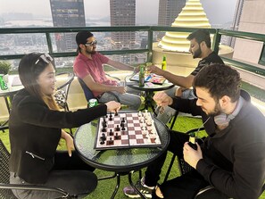 A group of people playing chess on a glass-top table with a city view in the background. - Wanderlust Partition Room in Barsha (Dubai)
