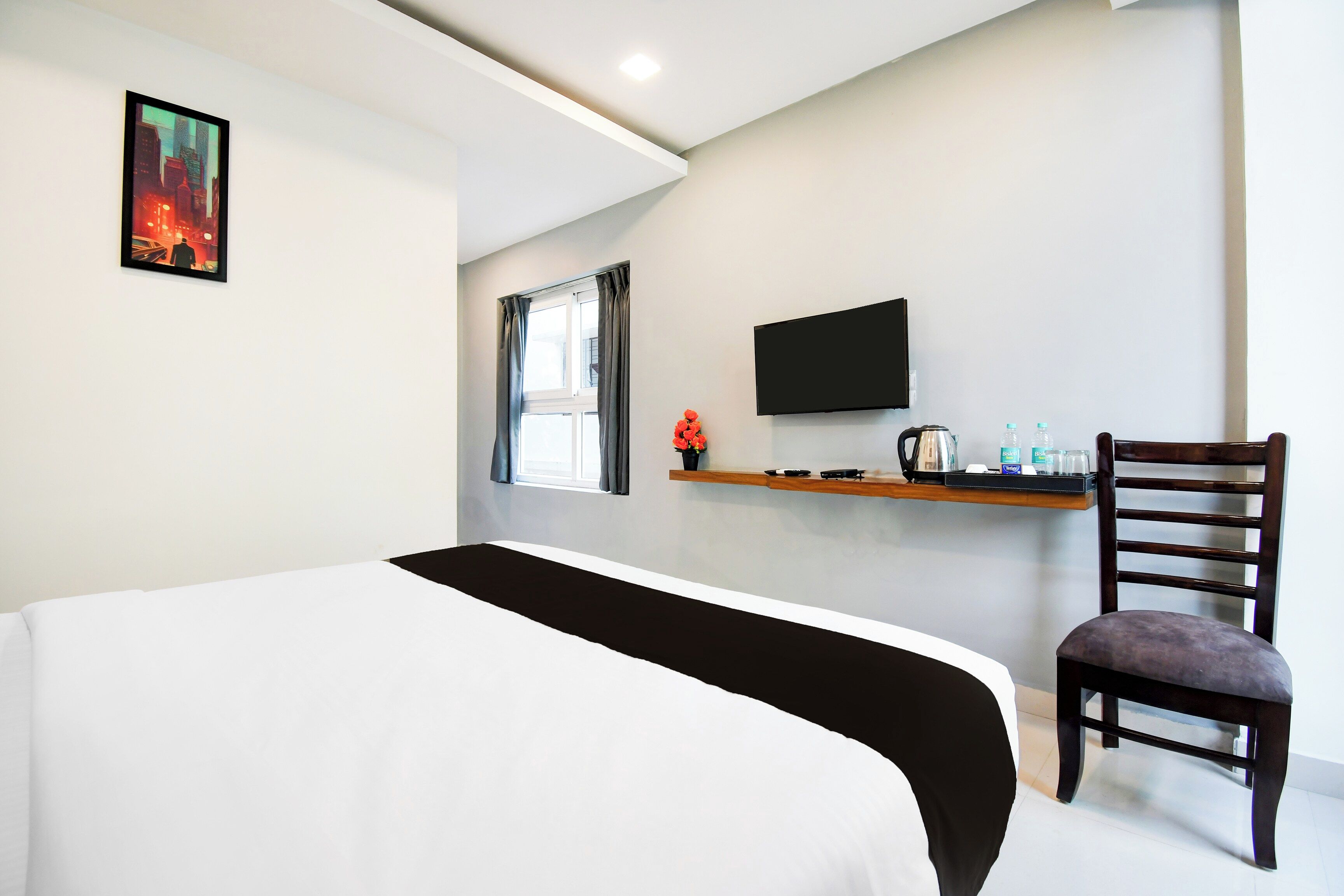 Ein Hotelzimmer mit einem Bett, einem Schreibtisch, einem Flachbildfernseher, einem Sessel und einem Fenster mit Vorhängen.