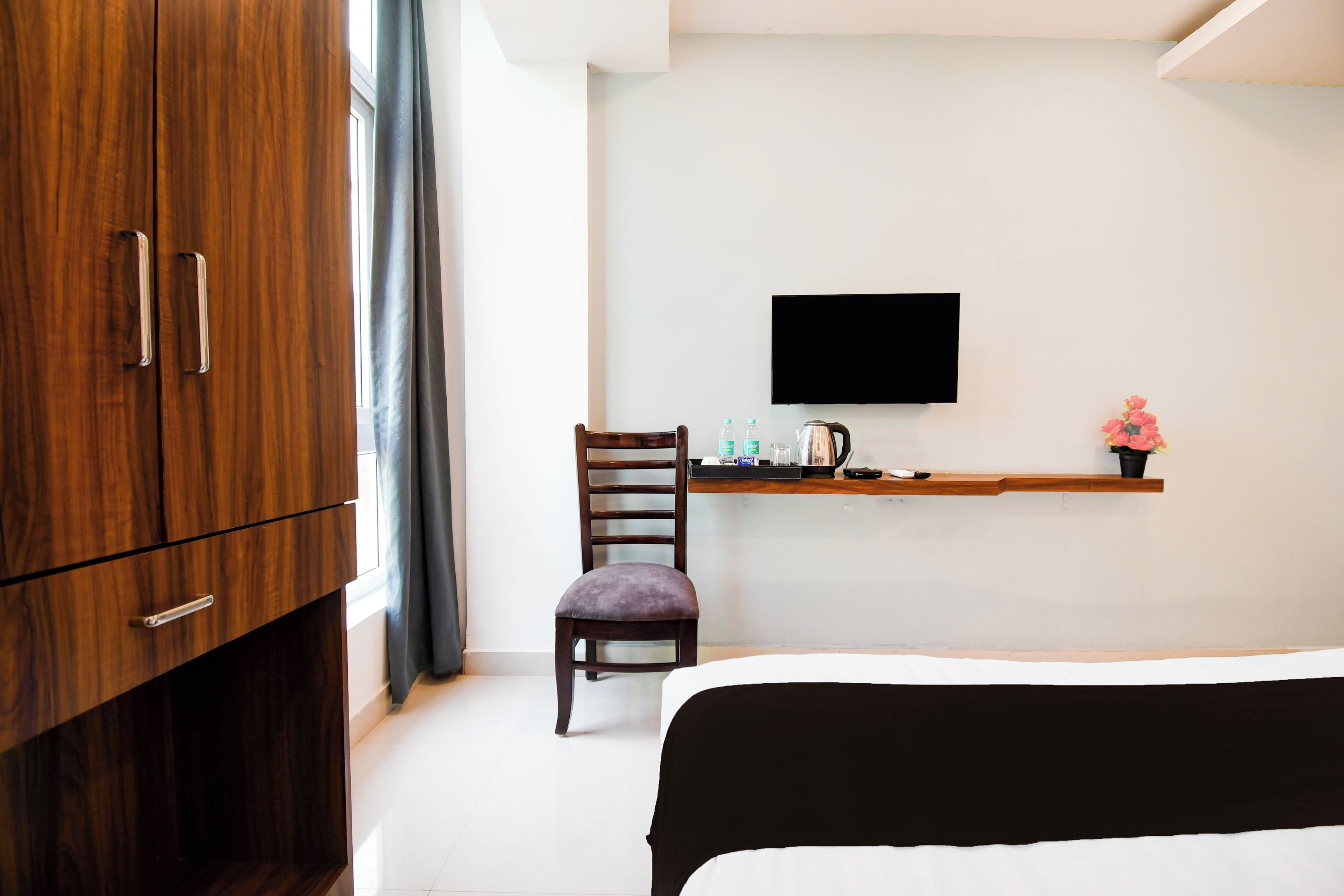 A hotel room with a bed, a desk with a flat-screen TV, a chair, and a wardrobe.