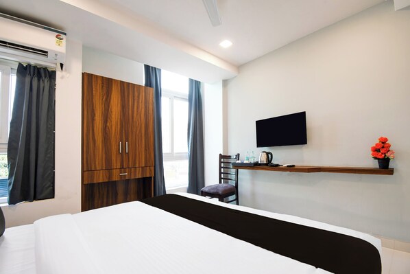 A hotel room with a bed, a TV mounted on the wall, a wooden wardrobe, and a window with curtains. - Townhouse Sayhallo Narcos (Bhubaneshwar)