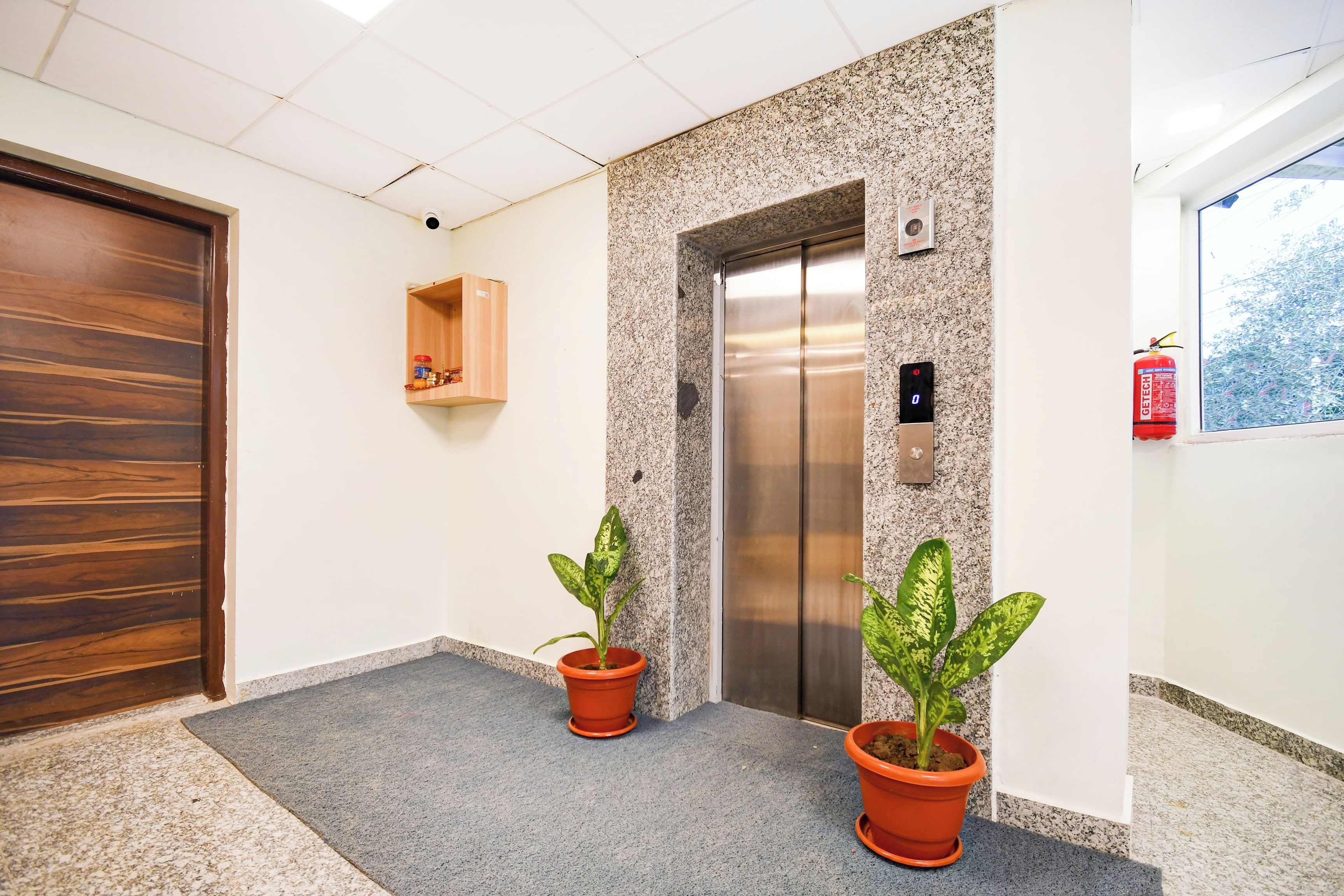 Um elevador com acabamento metálico, porta de madeira e uma prateleira com objetos.
