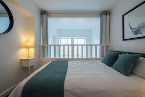 A hotel room with a bed, a nightstand, a lamp, a window with curtains, and a framed picture on the wall. - Bright Mezzanine One Bedroom Central Apartment (Edinburgh)