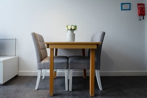 A dining area with a wooden table and two grey upholstered chairs. A white vase with flowers is on the table. - Bright Mezzanine One Bedroom Central Apartment (Edinburgh)