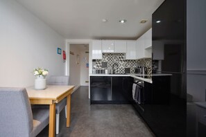 A compact kitchen with a black refrigerator, a coffee machine, and a tiled backsplash. - Bright Mezzanine One Bedroom Central Apartment (Edinburgh)