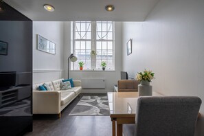 Un salon moderne avec un canapé, une table à manger et un téléviseur. On peut voir des plantes sur le rebord de la fenêtre et une lampe sur la table.