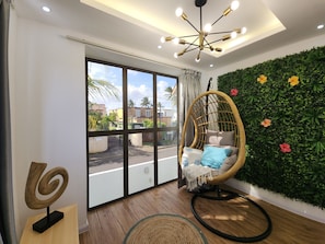 A room with a large sliding glass door, a wicker chair with cushions, a green wall with plants, and a ceiling light fixture. - Villa Palmito : 3-Bedroom Private Pool Villa in Trou aux Biches with AC (Trou aux Biches)