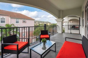 Ein Balkon mit Gartenmöbeln, einem Glastisch und Blick auf angrenzende Gebäude.