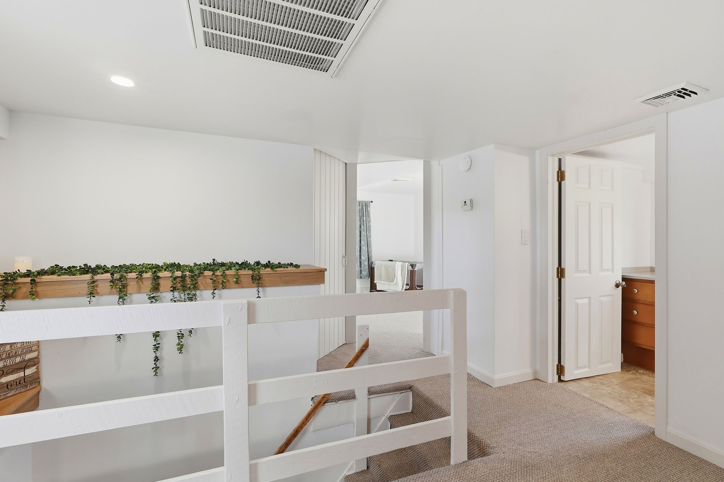 A modern, well-lit hallway with a white bench, a wooden shelf with greenery, and a door leading to another room.