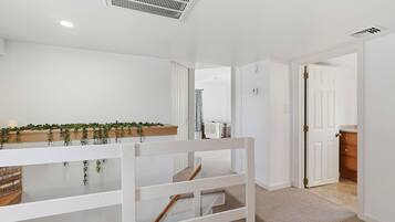 A modern, well-lit hallway with a white bench, a wooden shelf with greenery, and a door leading to another room.