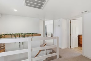 A modern, well-lit hallway with a white bench, a wooden shelf with greenery, and a door leading to another room.