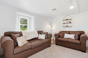 A living room with two brown leather sofas, a white throw blanket, and a white wall with a window.