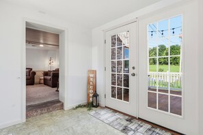 A clean, modern entrance with a white door, a welcome sign, and a view of a green lawn through the windows.