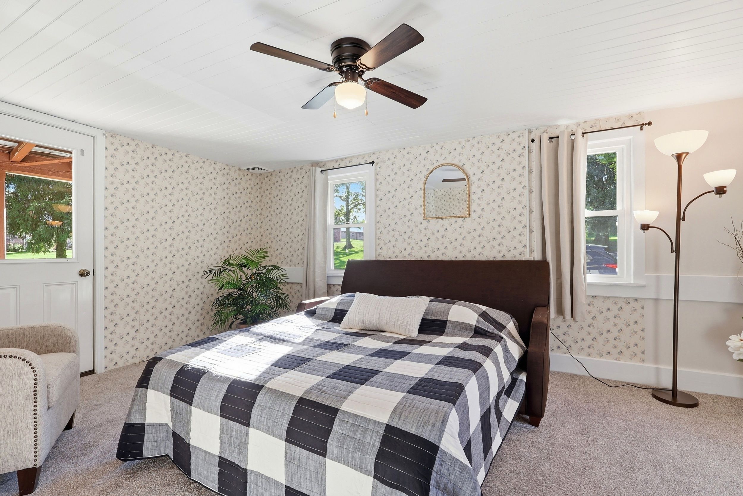Un dormitorio con cama, ventilador de techo, ventana con cortinas, lámpara de pie y puerta.