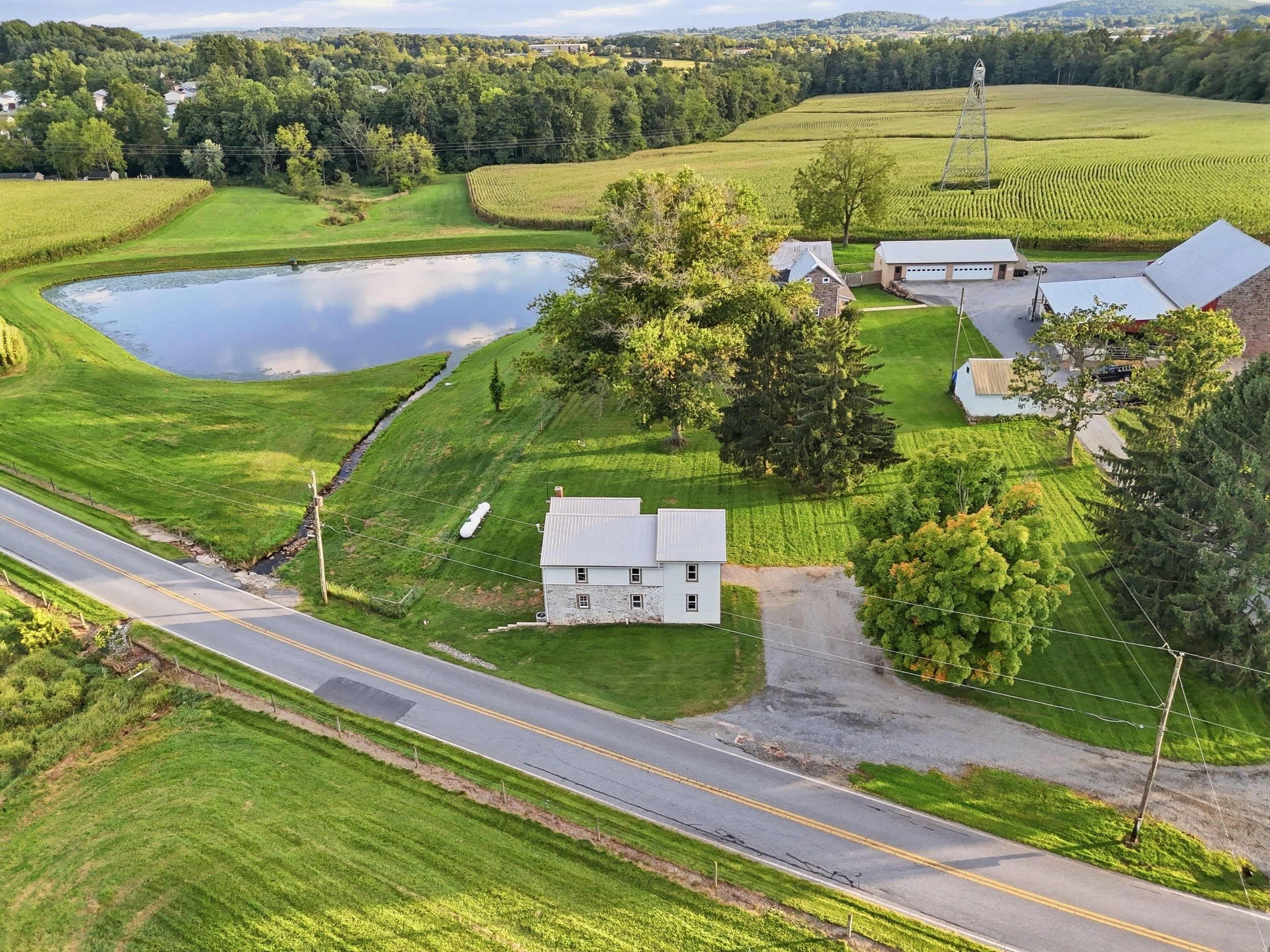 A rural landscape with a pond, a road, and a house with a garage.