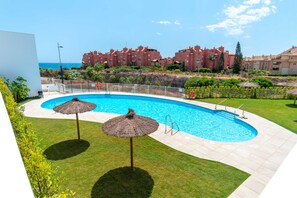 A swimming pool with two umbrellas, surrounded by a well-maintained lawn and a view of a coastal building complex. - Sea Blue Torrox Costa by Casasol (Torrox)