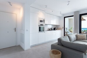 A modern kitchen with white cabinetry, built-in appliances, and a grey sofa in a living area with a view. - Sea Blue Torrox Costa by Casasol (Torrox)