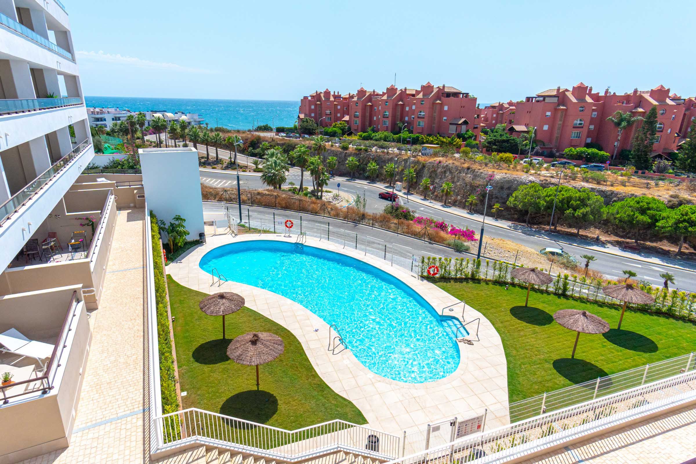 Una piscina de disseny corbat, envoltada per un solàrium blanc i algunes palmeres.