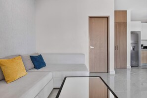 A modern living room with a sofa, a coffee table, and a door leading to a kitchen area. - Distrito Corazón: Bright 1BR w/ Balcony & Pool (Playa del Carmen)