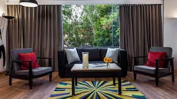 Quarto com sofá preto, duas poltronas, mesa de centro e tapete colorido.