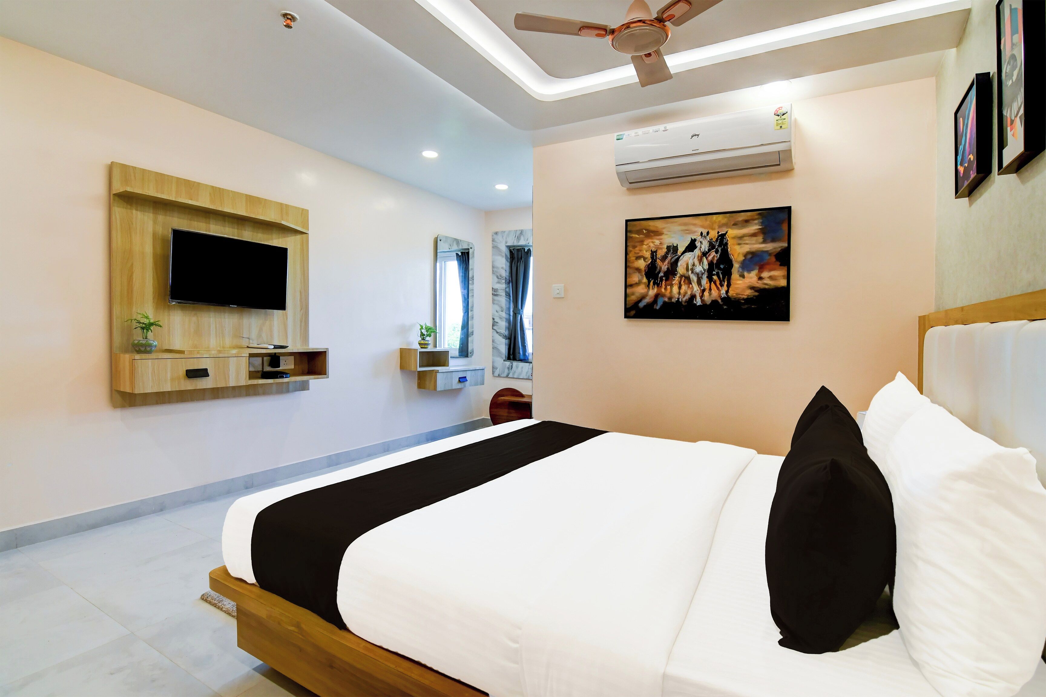 Quarto de hotel moderno com uma cama grande, televisão montada, ventilador de teto e obras de arte nas paredes.