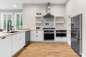 A modern kitchen with white cabinetry, a stainless steel range hood, and a built-in oven. - The Chestnut House (Tomball)