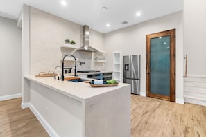 A modern kitchen with a central island, built-in appliances, and a wooden floor. - The Chestnut House (Tomball)