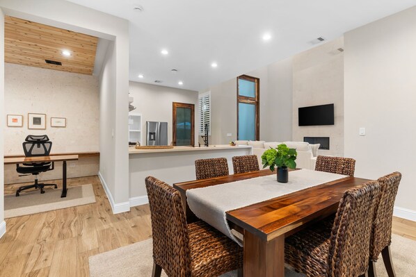 A modern dining area with a wooden table, woven chairs, and a central plant. - The Chestnut House (Tomball)