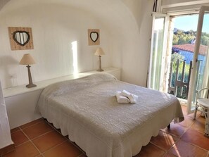 Une chambre à coucher avec un lit, deux lampes de chevet, une fenêtre donnant sur un beau paysage et un balcon.