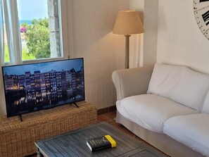 A living room with a television on a stand, a white sofa, a lamp, and a book on a coffee table. - Li Conchi Villa 17 - detached villa within the Li Conchi Village (Castiadas)