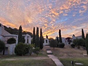A courtyard with stone buildings, cypress trees, and a pathway leading to a structure. - Li Conchi Villa 17 - detached villa within the Li Conchi Village (Castiadas)
