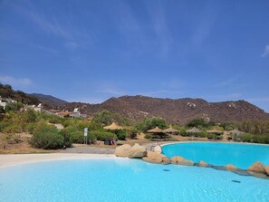 A clear blue pool with rocks, surrounded by greenery and a mountain in the background. - Li Conchi Villa 17 - detached villa within the Li Conchi Village (Castiadas)