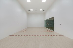 Ein geräumiger Squashplatz im Innenbereich mit Holzboden und roten Spiellinien.