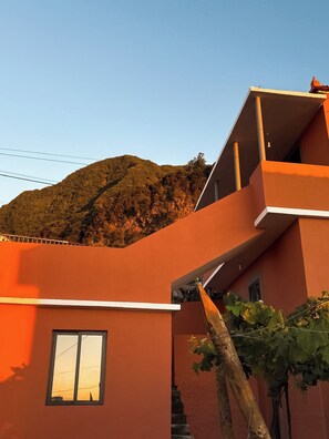 Un bâtiment moderne doté d’un toit plat et d’un balcon, situé au milieu d’un paysage vallonné.