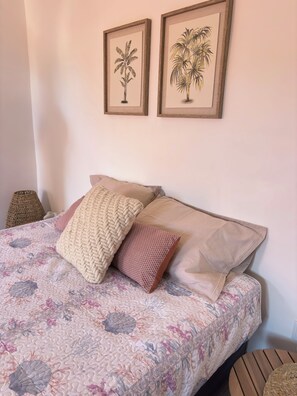 A bed with a floral-patterned bedspread, two framed botanical prints on the wall, and a woven basket beside the bed. - Casa do Portinho - Country house with a spectacular view of the Atlantic Ocean (Ponta Delgada)