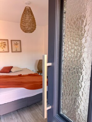 Une chambre à coucher avec un lit, des oreillers, une couverture, un mur à texture et un luminaire suspendu.