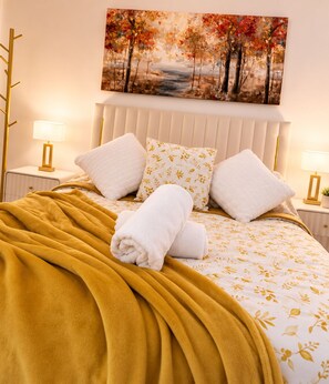 Cama bem arrumada com colcha estampada, duas almofadas e uma toalha branca enrolada.