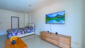 Un dormitorio con una cama, un aparador de madera, un televisor en la pared y un florero con flores sobre una mesa.