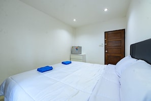 Um quarto com cama, porta de madeira, armário branco pequeno e geladeira.