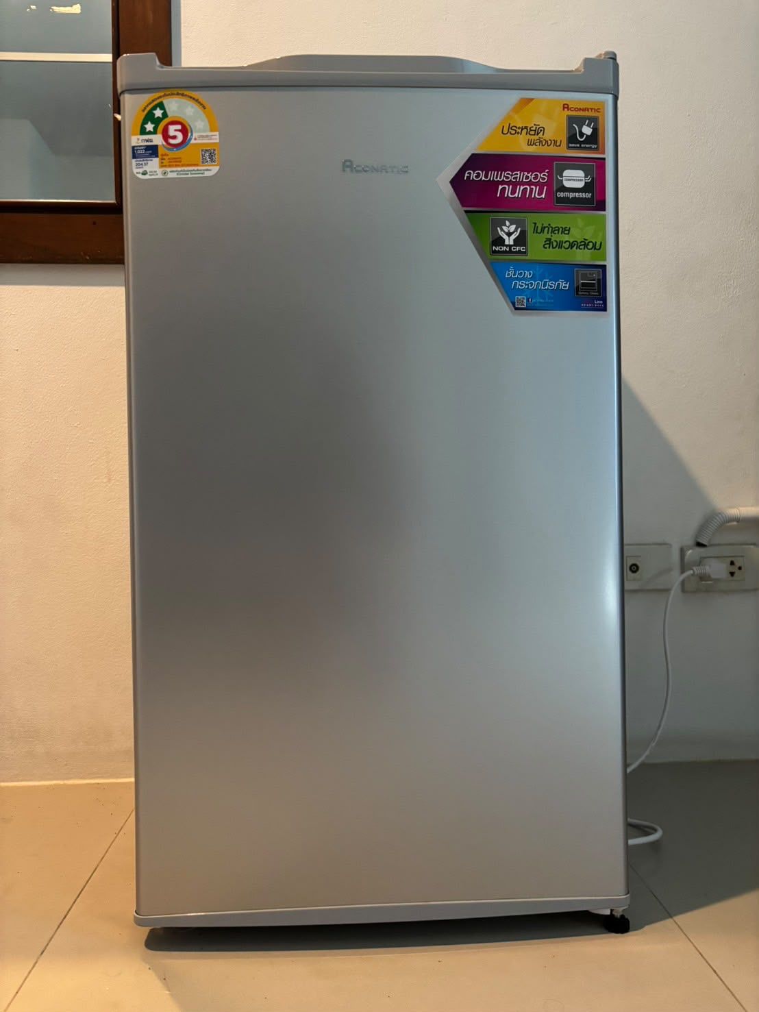A silver refrigerator with multiple stickers, including energy efficiency and safety certifications.