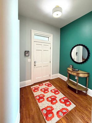 A hallway with a wooden floor, a white door, a teal wall, and a mirror on a wooden console. - Charming updated home w/large bedrooms & big deck. Great for groups & families! (Shelbyville)