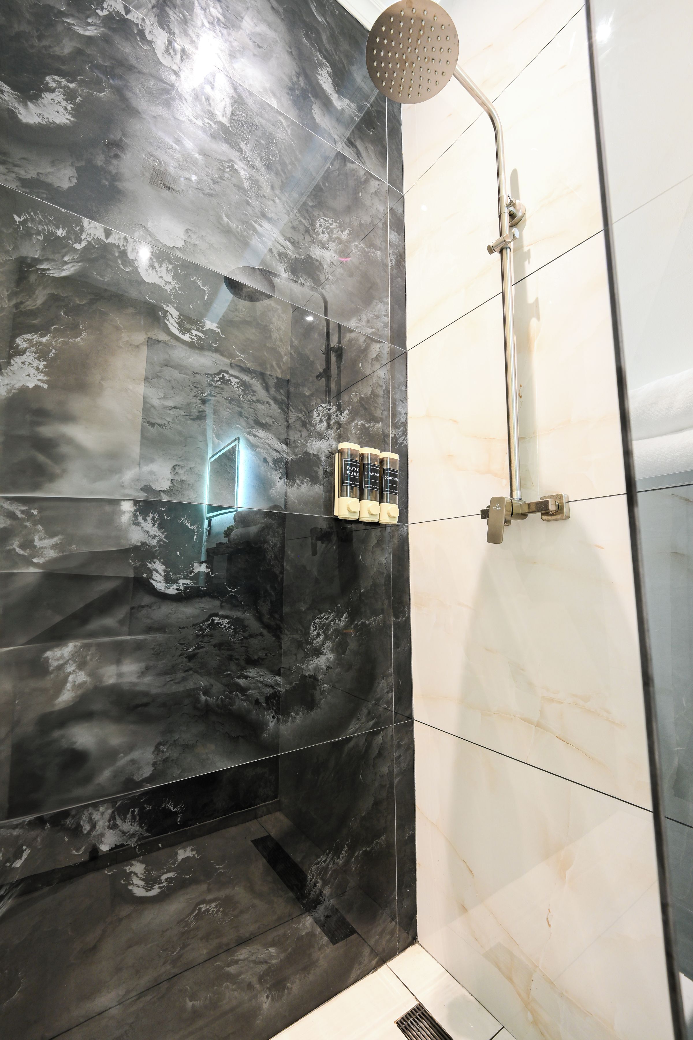 A modern bathroom with a shower, marble walls, and toiletries.