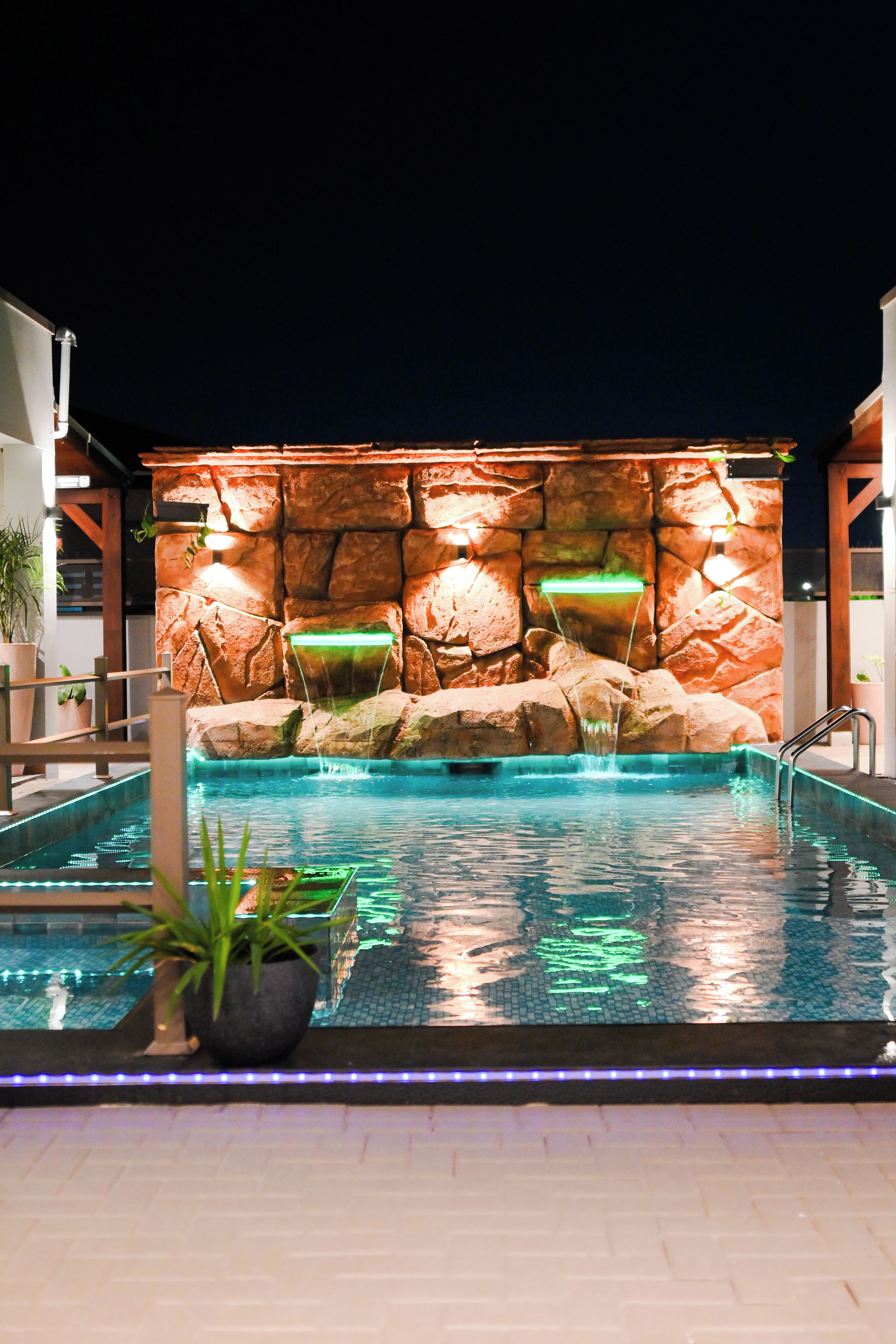 A swimming pool with a rock waterfall feature and a night-time setting.