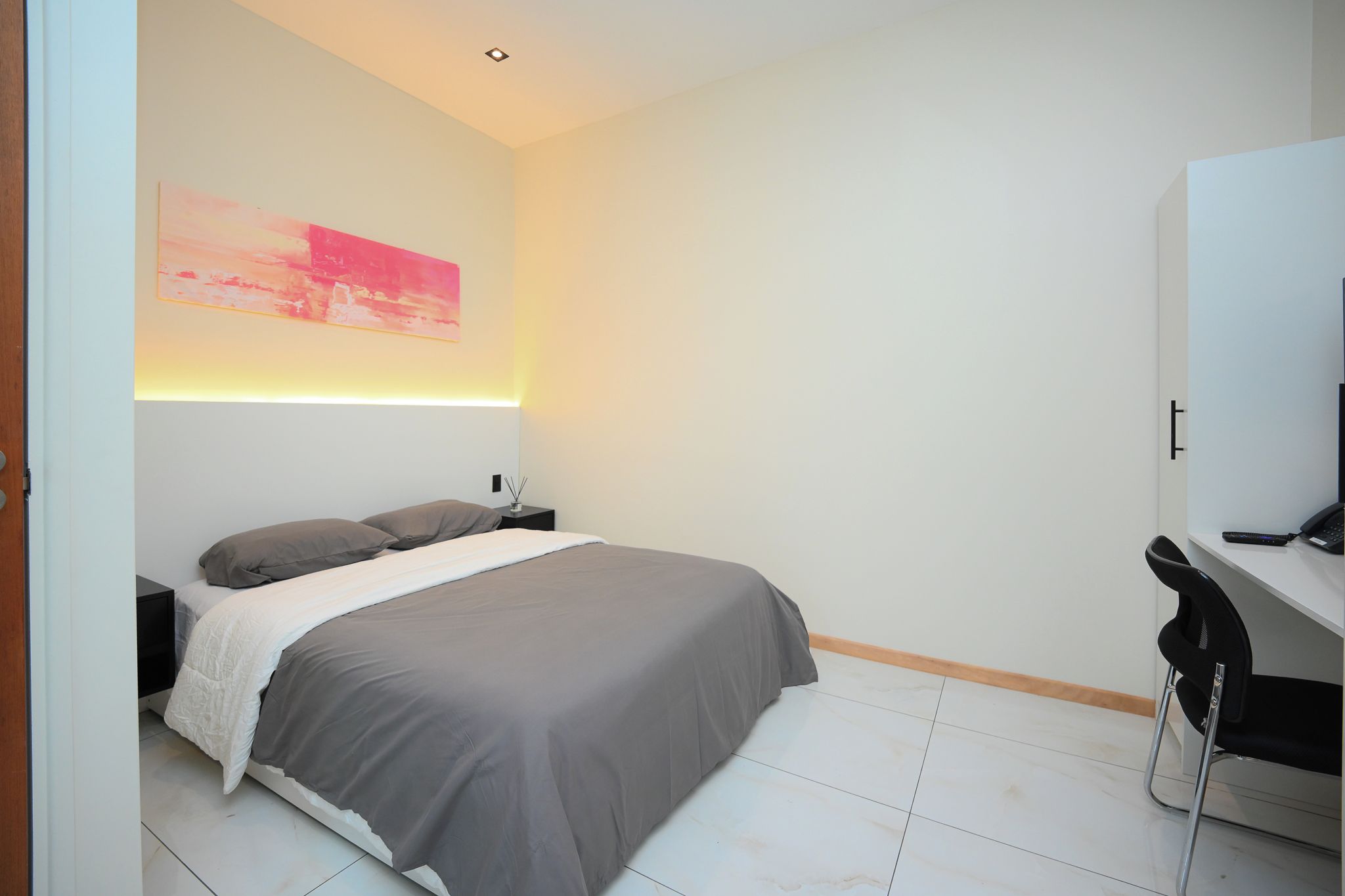 A modern bedroom with a bed, bedside table, and a desk with a chair.