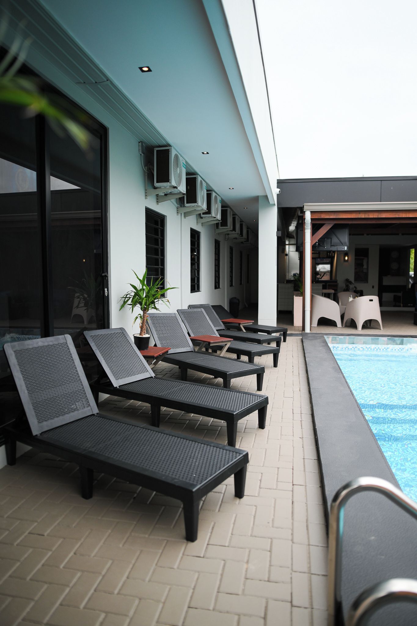 Área de piscina externa com espreguiçadeiras e um vaso de planta.