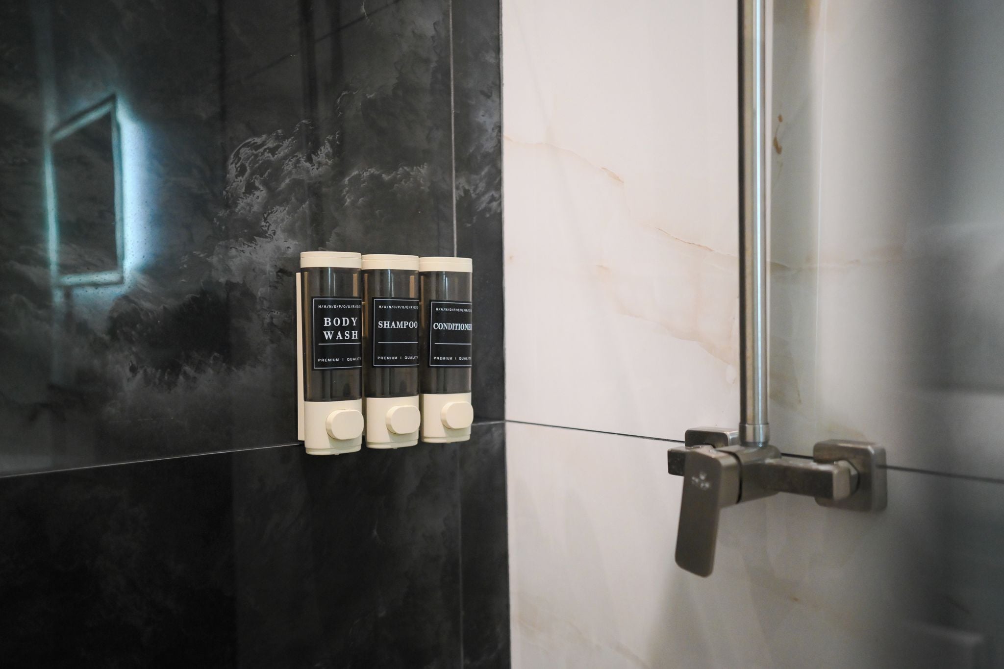Um banheiro com parede revestida de azulejos preto e branco, porta de chuveiro e três frascos de sabonete líquido, shampoo e condicionador.
