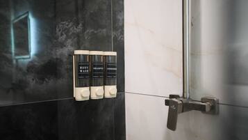 Um banheiro com parede revestida de azulejos preto e branco, porta de chuveiro e três frascos de sabonete líquido, shampoo e condicionador.